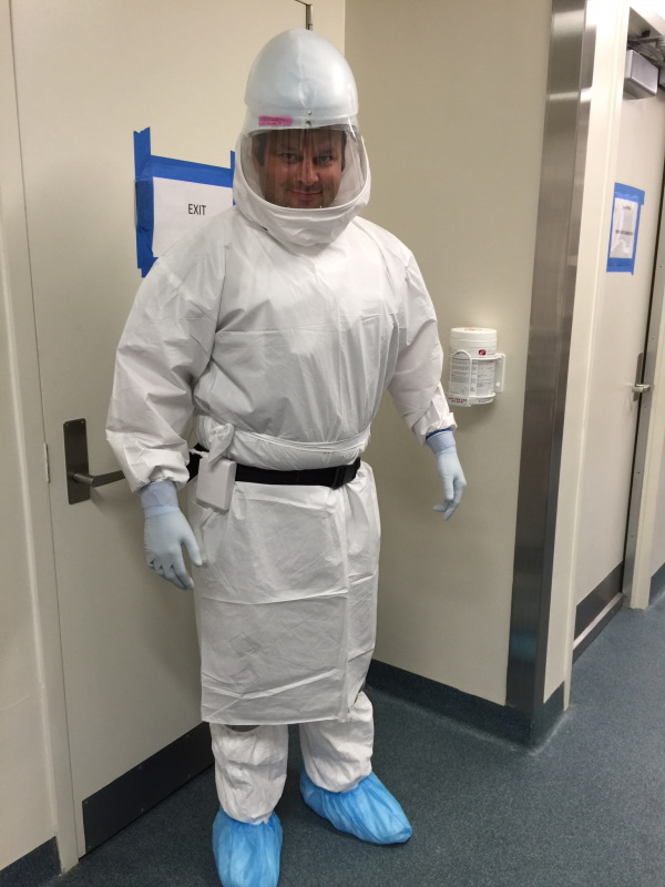 Person wearing full personal protective equipment including a hooded suit, gloves, and shoe covers standing in a hallway