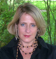 Person wearing a black shirt and beaded necklace posing against a background of green foliage