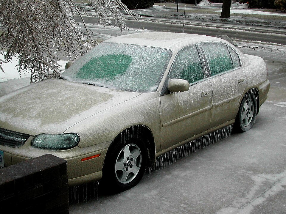 Picture of a car covered in ice from an ice storm. A tree leans over the car from the left.