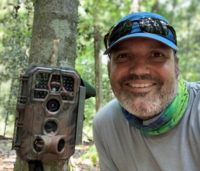 Dr. Blackburn smiling next to a wildlife camera.