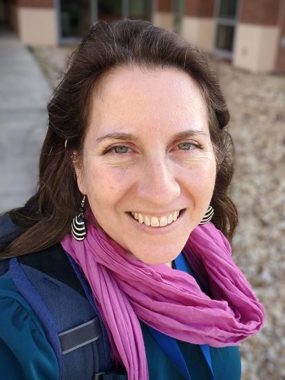 Headshot of Dr Sadie Ryan, wearing a pink scarf, grinning
