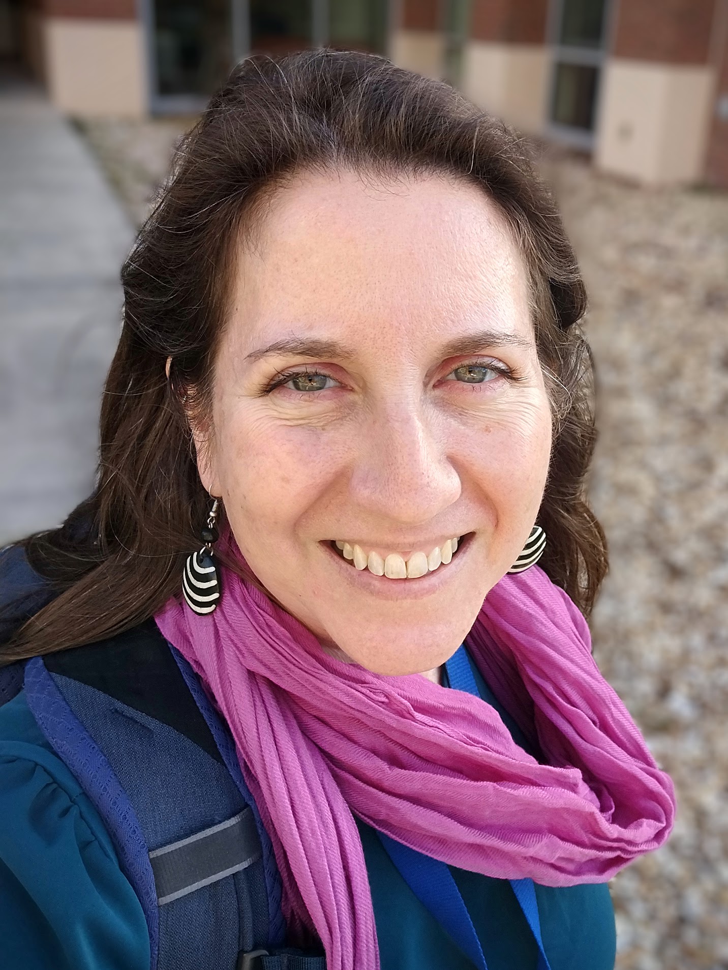 Headshot of Dr Sadie Ryan, wearing a pink scarf, grinning